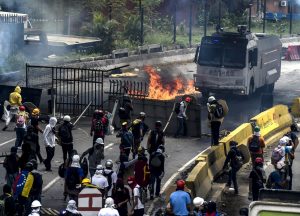 Opposition activists, equipped with helmets, gas masks, makeshift shields and barricaded behind debris, face charging riot police during a protest against Venezuelan President Nicolas Maduro, in Caracas on May 3, 2017. Venezuela's angry opposition rallied Wednesday vowing huge street protests against President Nicolas Maduro's plan to rewrite the constitution and accusing him of dodging elections to cling to power despite deadly unrest. / AFP PHOTO / JUAN BARRETO