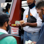 A bus driver’s assistant collects fares while holding a wad of Bolivar banknotes at a bus stop outside the Antimano metro station in Caracas